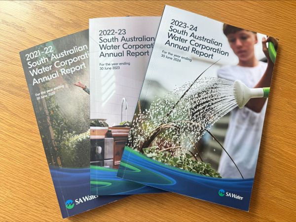 Three SA Water annual reports from 2021–22, 2022–23, and 2023–24 on a tabletop, with covers showing different people using water in domestic settings.